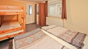 A room with two bunk beds, a wooden door, a window with curtains, and a radiator. - Ferienhaus Lubmin (Seebad) (Lubmin (Seebad))