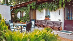 An outdoor seating area with a bench and chairs, surrounded by greenery and potted plants. - Ferienhaus Lubmin (Seebad) (Lubmin (Seebad))