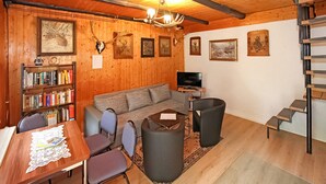 Ein gemütliches Wohnzimmer mit Holzvertäfelung, einer Couch, einem Couchtisch, einem Fernseher, einem Bücherregal und einer Treppe.