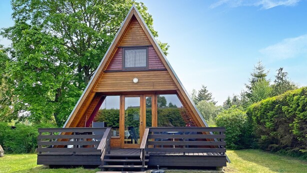 Una baita a forma di A in legno, con ingresso tramite porta in vetro e un piccolo portico.