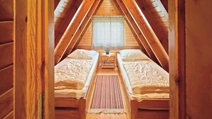 Una camera mansardata con due letti singoli, un tavolino e una finestra con tenda decorata.