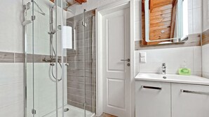 Un bagno moderno con doccia vetrata, un lavabo bianco con dispenser per sapone e uno specchio con cornice in legno sopra il lavabo.