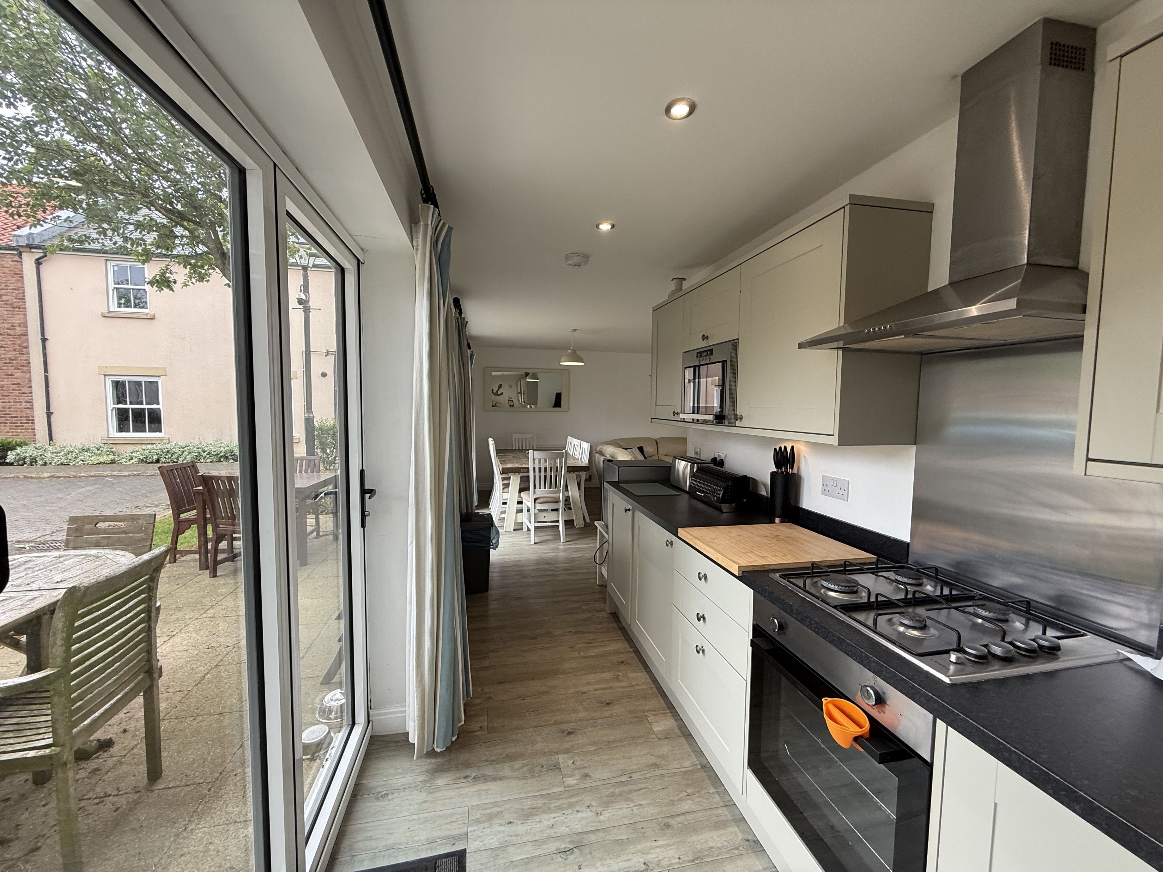 A modern kitchen with a large window, a dining area with a table and chairs, and a view of a building outside.