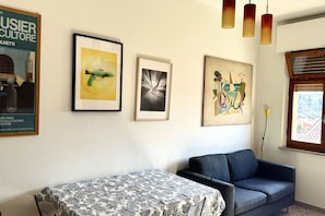 Una habitación con un sofá, una mesa con mantel estampado y tres cuadros en la pared.