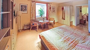 A bedroom with a bed, a desk, two chairs, a window with curtains, a radiator, and a wardrobe. - Ferienwohnung Wokuhl-Dabelow (Wokuhl-Dabelow)