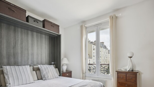 A bedroom with a bed, bedside table, dresser, and a window with a view of buildings. - Studio St Dominique - Invalides - B'Your Home (Paris)