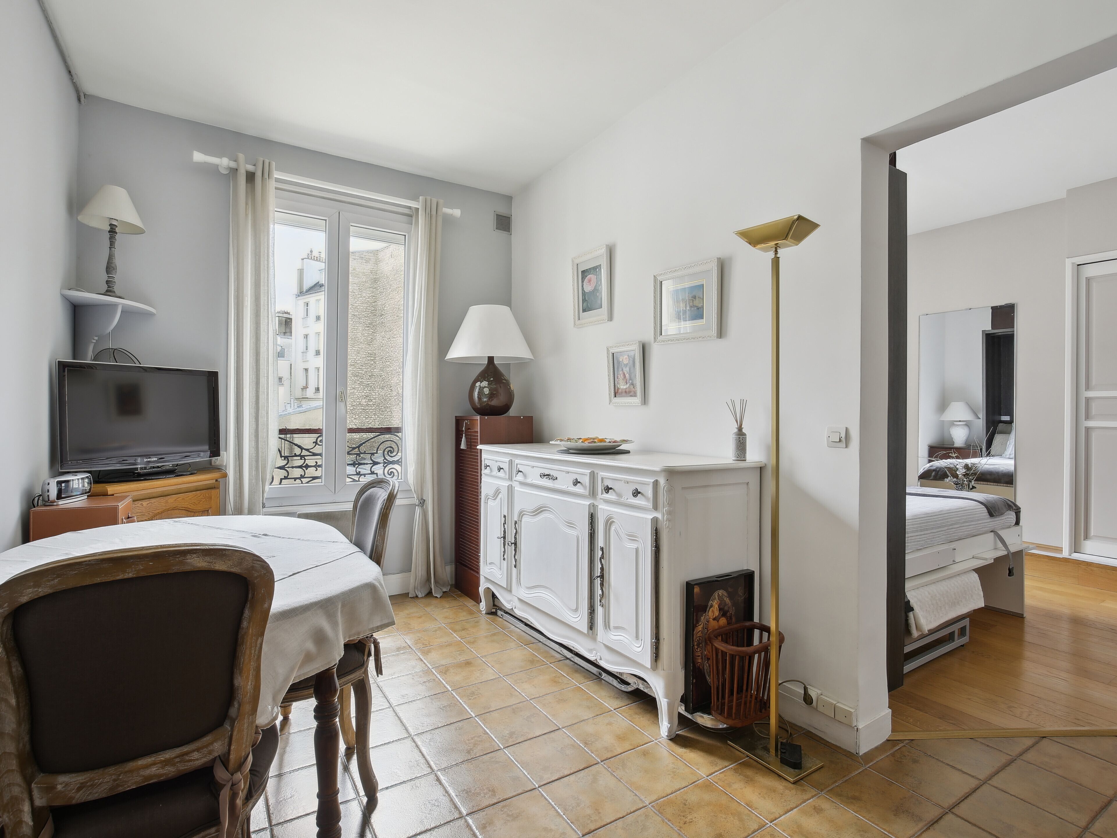 A compact hotel room with a bed, a dining area with a table and chairs, a TV, a cabinet, and a window with curtains.