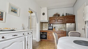 A compact kitchen with white cabinetry, a dining area with a table, and a tiled backsplash. - Studio St Dominique - Invalides - B'Your Home (Paris)