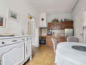 A compact kitchen with white cabinetry, a dining area with a table, and a tiled backsplash.