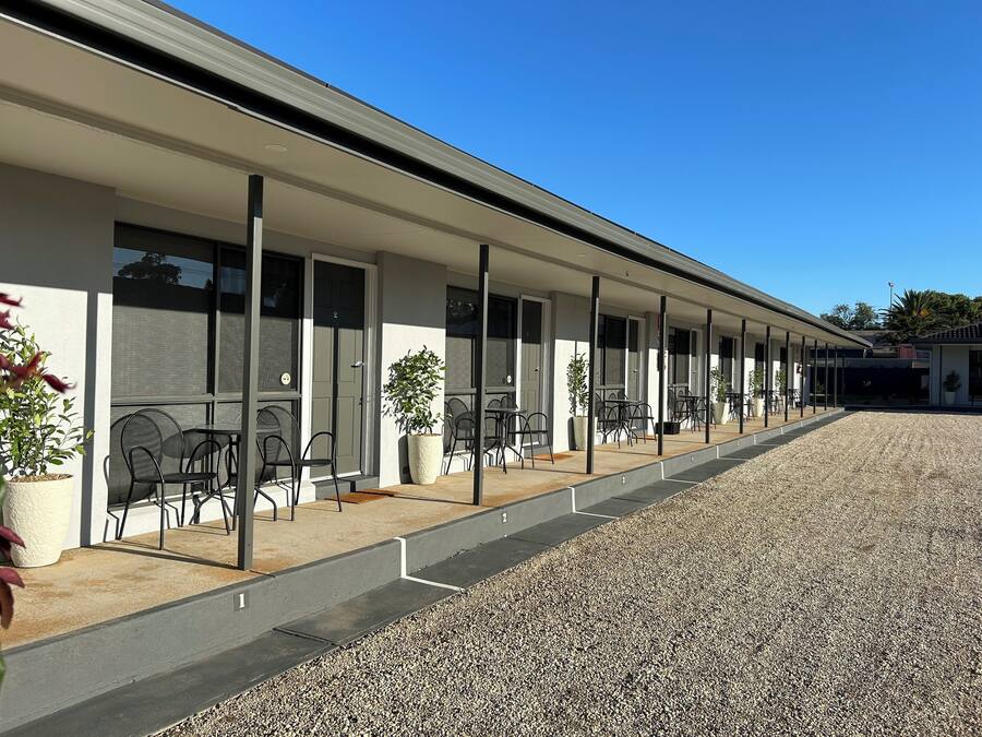 Un motel moderne doté d’un espace extérieur aménagé avec des places assises, de chambres individuelles avec des portes coulissantes et une allée gravillonnée.