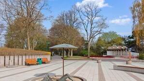 A public square with a sculpture, benches, a covered pavilion, and a building with a unique architectural design. - Ferienwohnung Karlshagen (Karlshagen (Ostseebad))