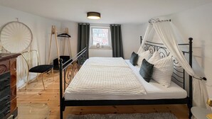 A bedroom with a bed, a chair, a dresser, and a window with curtains. - Ferienwohnung Rheinsberg (Rheinsberg)