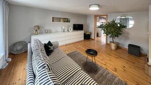 A modern living room with a striped sofa, a small round table, a TV, a white cabinet, and a potted plant. - Ferienwohnung Rheinsberg (Rheinsberg)