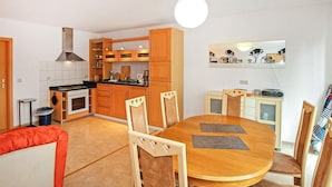 A compact kitchen with wooden cabinets, a stove, and a dining area with a wooden table and chairs. - Ferienwohnung Walow Strietfeld (Walow OT Strietfeld)
