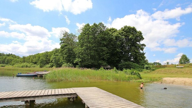 A wooden dock extending into a calm body of water, surrounded by lush greenery and trees. - Ferienwohnung Walow Strietfeld (Walow OT Strietfeld)