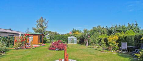 A well-maintained garden with a circular stone feature, a wooden shed, and a greenhouse.