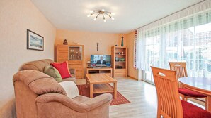 Ein Wohnzimmer mit einer Couch, einem Fernseher, einem Holzschrank und einem Essbereich mit Stühlen und einem Tisch.