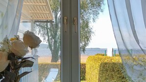 A room with a view of a lake, a chair, and a vase with flowers.