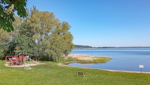 A lakeside park with playground equipment, a bench, and a sign indicating a no swimming area.
