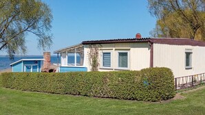 A small, single-story house with a blue and white exterior, a covered porch, and a view of the water.