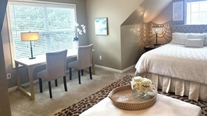 Une chambre à coucher comprenant un lit, un bureau avec des chaises, un ventilateur de plafond et une fenêtre avec des stores.