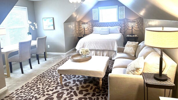 Une chambre avec un lit, un bureau et une chaise. On y trouve un ventilateur de plafond, une lampe et un tapis à motifs léopard.