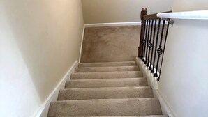 Un escalier recouvert de moquette, avec un tableau accroché au mur au-dessus.