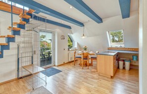 Moderni keittiö, jossa on ruokailutila, puinen portaikko ja suuret ikkunat.