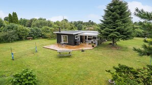 Ett litet, modernt hus med en veranda, ett område för grillning och en uteplats.
