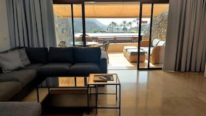 Sala de estar moderna com sofá seccional, uma mesinha de centro e vista para um pátio com mobiliário externo e montanhas ao fundo.