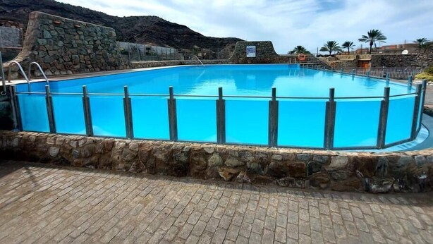 Piscina retangular com uma parede de pedra ao redor, com montanhas ao fundo.