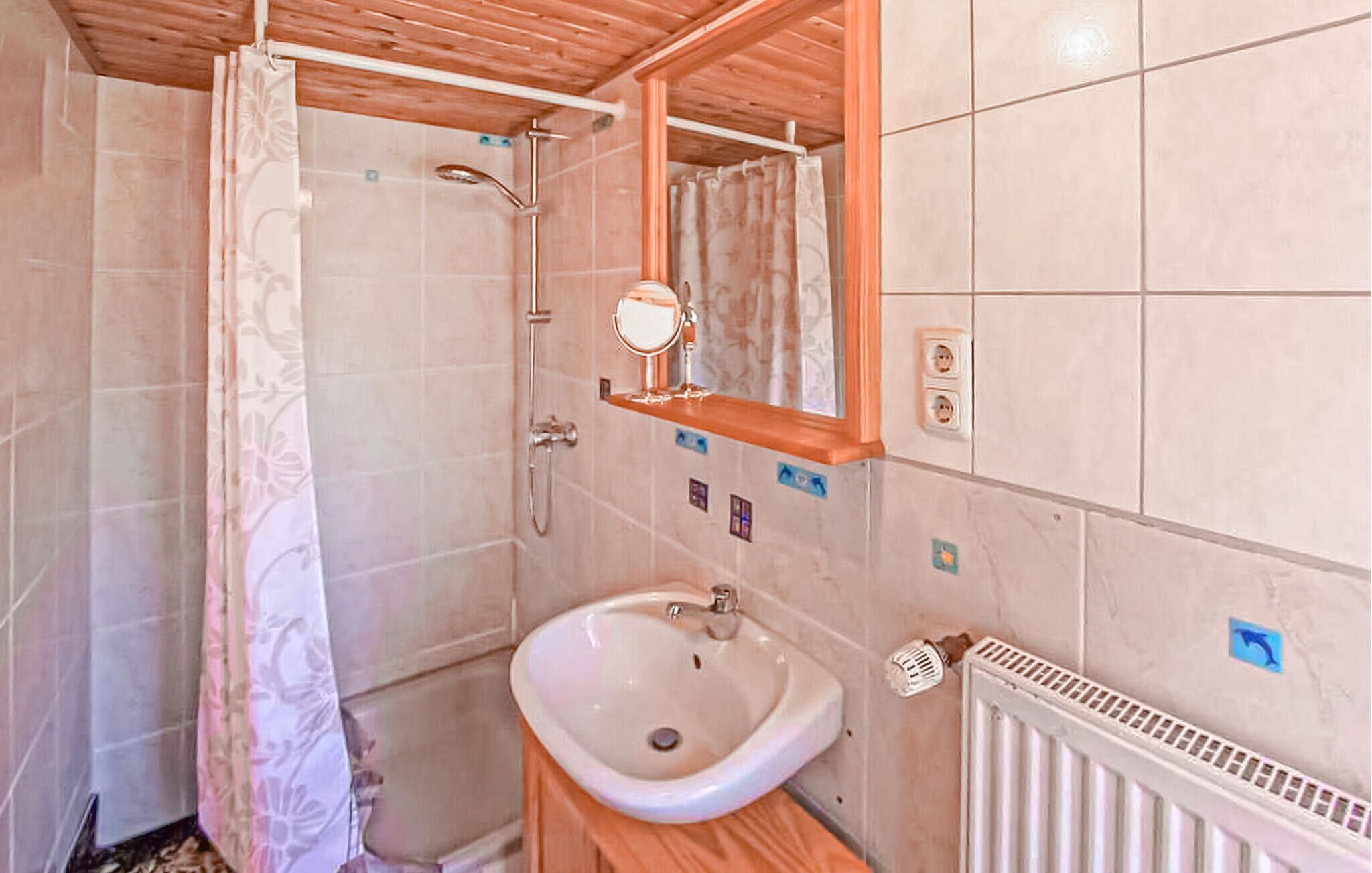 Une salle de bain équipée d’une douche, d’un lavabo, d’un miroir et d’un radiateur.