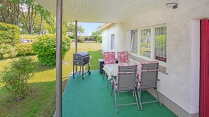 Une terrasse couverte avec une table et des chaises, un barbecue et une vue sur le jardin.