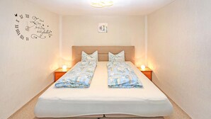 Une chambre à coucher avec un lit, deux tables de chevet, une horloge murale et un petit tableau.