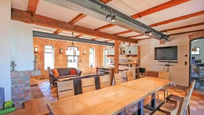 A spacious living area with a large wooden table, comfortable seating, and a brick wall.