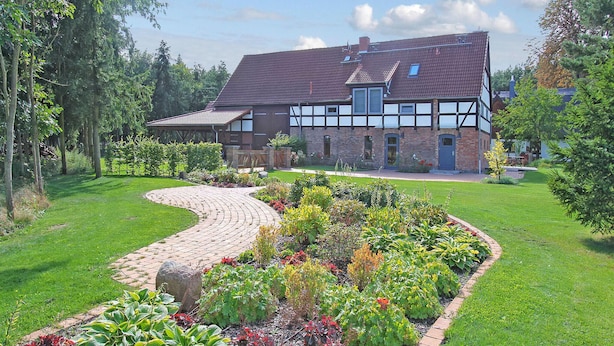 A large house with a paved driveway and a garden with various plants.