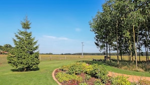 A well-maintained garden with a variety of plants and a lawn, a tall metal structure, and a clear blue sky.