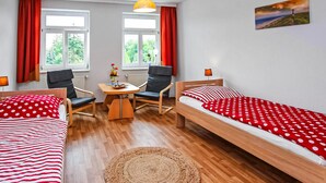 Une chambre avec deux lits simples, une table en bois, deux chaises, une lampe et une fenêtre avec des rideaux.