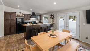 A spacious kitchen with dark wooden cabinets, a central island, and a dining area with a wooden table and chairs. - Dreamcatcher (West Yellowstone)