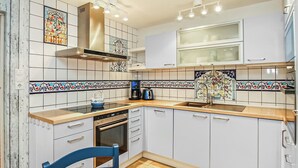 Une cuisine avec des armoires blanches, une hotte de cuisinière en acier inoxydable, un évier à deux bacs et une chaise bleue.