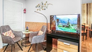Un salon moderne doté d’un téléviseur à écran plat, de deux fauteuils gris ornés de coussins à motifs floraux, d’une table basse en bois et d’un élément décoratif mural.