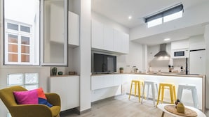 Una cocina moderna con armarios blancos, una isla central con taburetes y un ventanal luminoso.