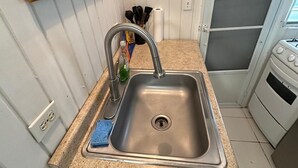 A kitchen with a stainless steel sink, a countertop, a stove, and a wooden cabinet with a framed picture.