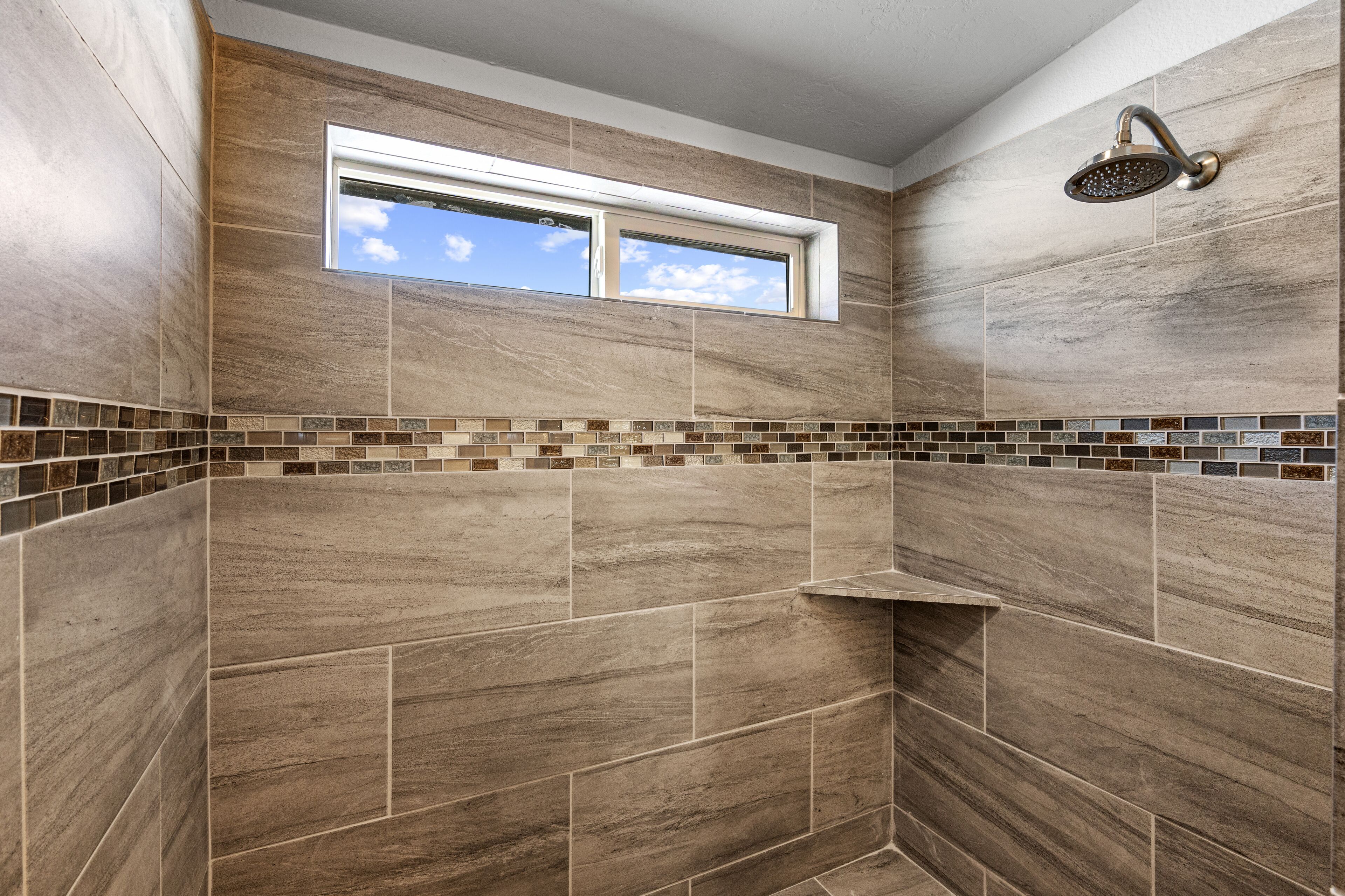 A shower with a window above, tiled walls, and a small shelf.
