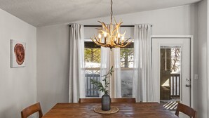 Ein Essbereich mit Holztisch, Stühlen, einer Chandelierleuchtre und einem Blumentopf.