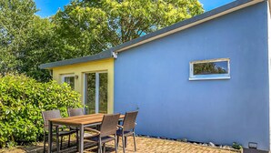 A patio with a table and chairs, a small building with a window, and a blue wall.