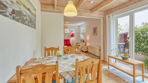 A dining area with wooden furniture, a table set for four, and a view of the outdoors through large windows.