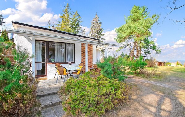 Une petite maison avec un patio, une table et des chaises, et une vue sur les arbres et le ciel environnants.