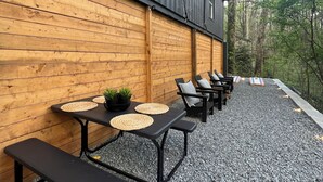 An outdoor seating area with tables and benches, a wooden wall, and a gravel ground.