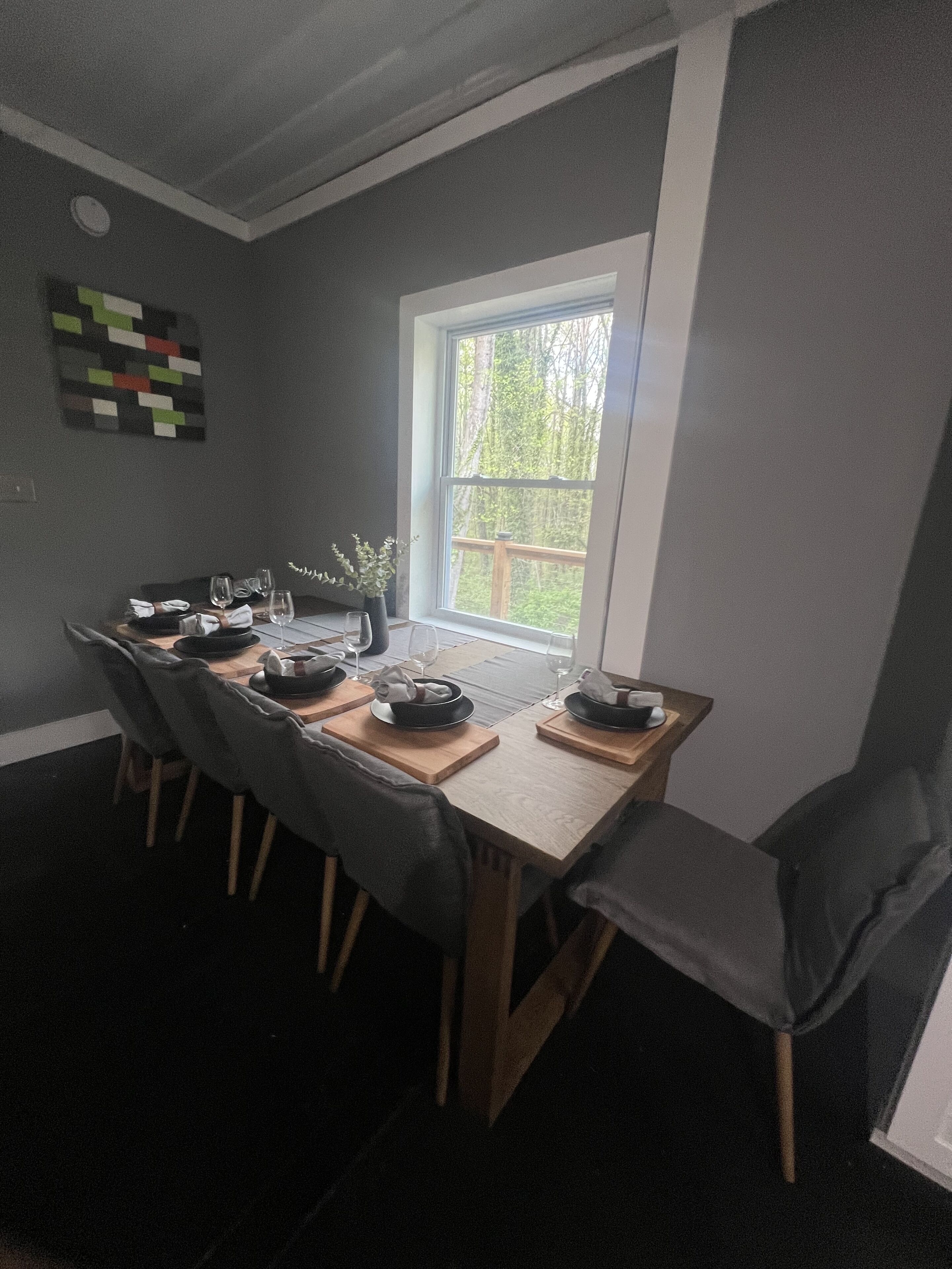Un comedor con una mesa dispuesta para cuatro, sillas de madera y una ventana con vistas a árboles.